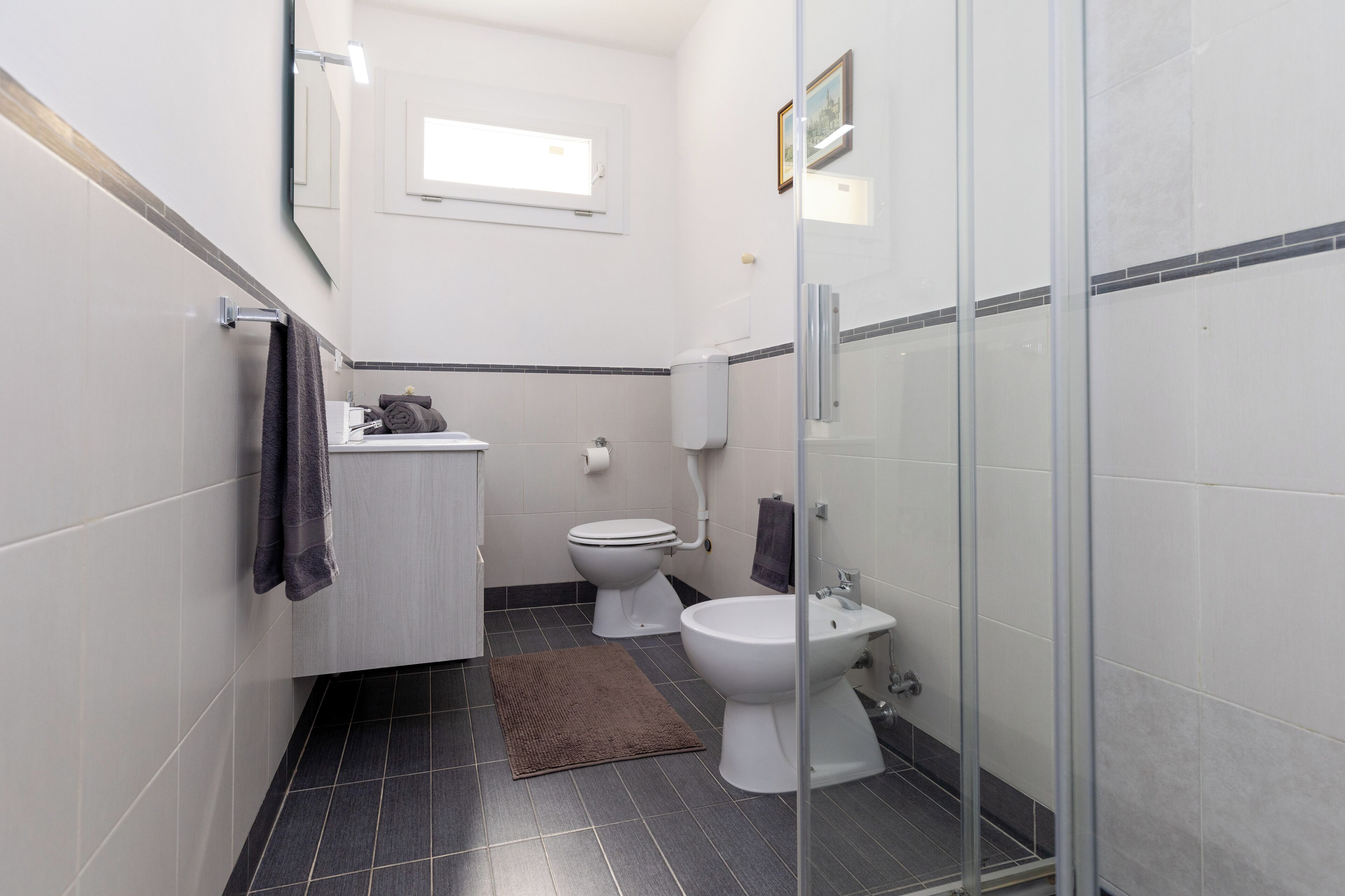 A compact bathroom with a toilet, bidet, and a glass shower enclosure.