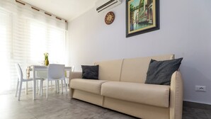Un soggiorno con un divano color beige, due cuscini decorati, un tavolo da pranzo con sedie, un vaso con fiori e un quadro appeso al muro.
