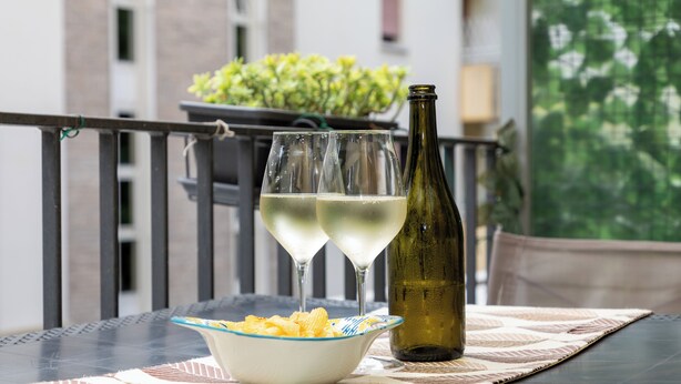 Un tavolo con due bicchieri di vino bianco, una bottiglia e una ciotola di patatine su un sottopiattino decorato.