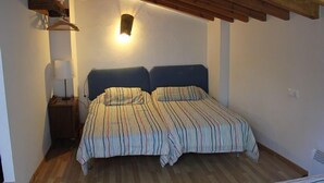 A bedroom with a wooden ceiling, a bed with striped bedding, a bedside table with a lamp, and a wall-mounted light fixture.