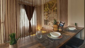 A dining area with a wooden table, a woven partition, and a small plant. - Kazette - Your Holiday Studio on Reunion Island (L'Étang Saint-Louis)