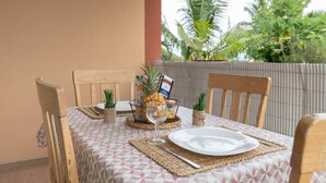 An outdoor dining area with a table set for two, featuring a pineapple, a wine glass, and a menu. - Kazette - Your Holiday Studio on Reunion Island (L'Étang Saint-Louis)