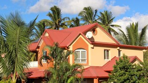 A two-story building with a red roof and beige walls, surrounded by palm trees. - Kazette - Your Holiday Studio on Reunion Island (L'Étang Saint-Louis)
