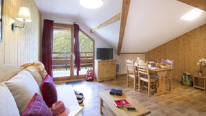 Um quarto aconchegante com teto de madeira, um sofá com almofadas, uma mesa de jantar com cadeiras, uma televisão e uma janela com cortinas.