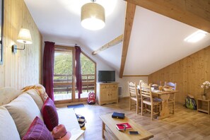 A cozy room with a wooden ceiling, a sofa with cushions, a dining table with chairs, a TV, and a window with curtains. - Rustic apartment with dishwasher in Valmeinie (VALMEINIER)
