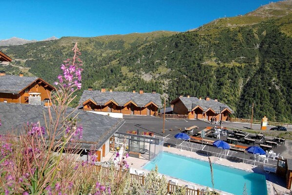 A mountain lodge with multiple chalet-style cabins, a swimming pool, and a view of the surrounding forested hills.