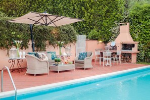 A poolside area with wicker furniture, a barbecue grill, and a lantern.