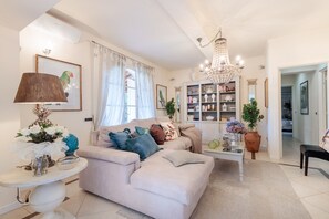 A living room with a sofa, a coffee table, a chandelier, and a bookshelf.