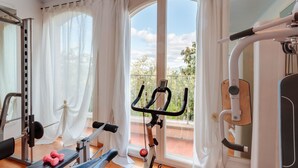 A home gym with a stationary bike, a bench press, and dumbbells. - Beautiful Villa Lory on the hills of Lucca (Segromigno in Monte)