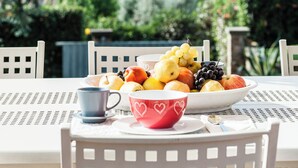 An outdoor dining table with a fruit bowl, two cups, and a view of trees and buildings in the background. - Beautiful Villa Lory on the hills of Lucca (Segromigno in Monte)