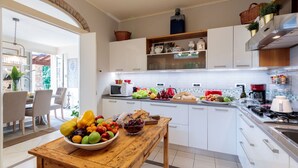 A modern kitchen with white cabinets, a wooden table with fruit, and a dining area with chairs. - Beautiful Villa Lory on the hills of Lucca (Segromigno in Monte)