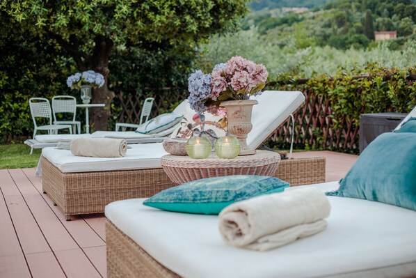 A sunlit outdoor seating area with wicker furniture, a white cushioned sofa, and a table with decorative items.
