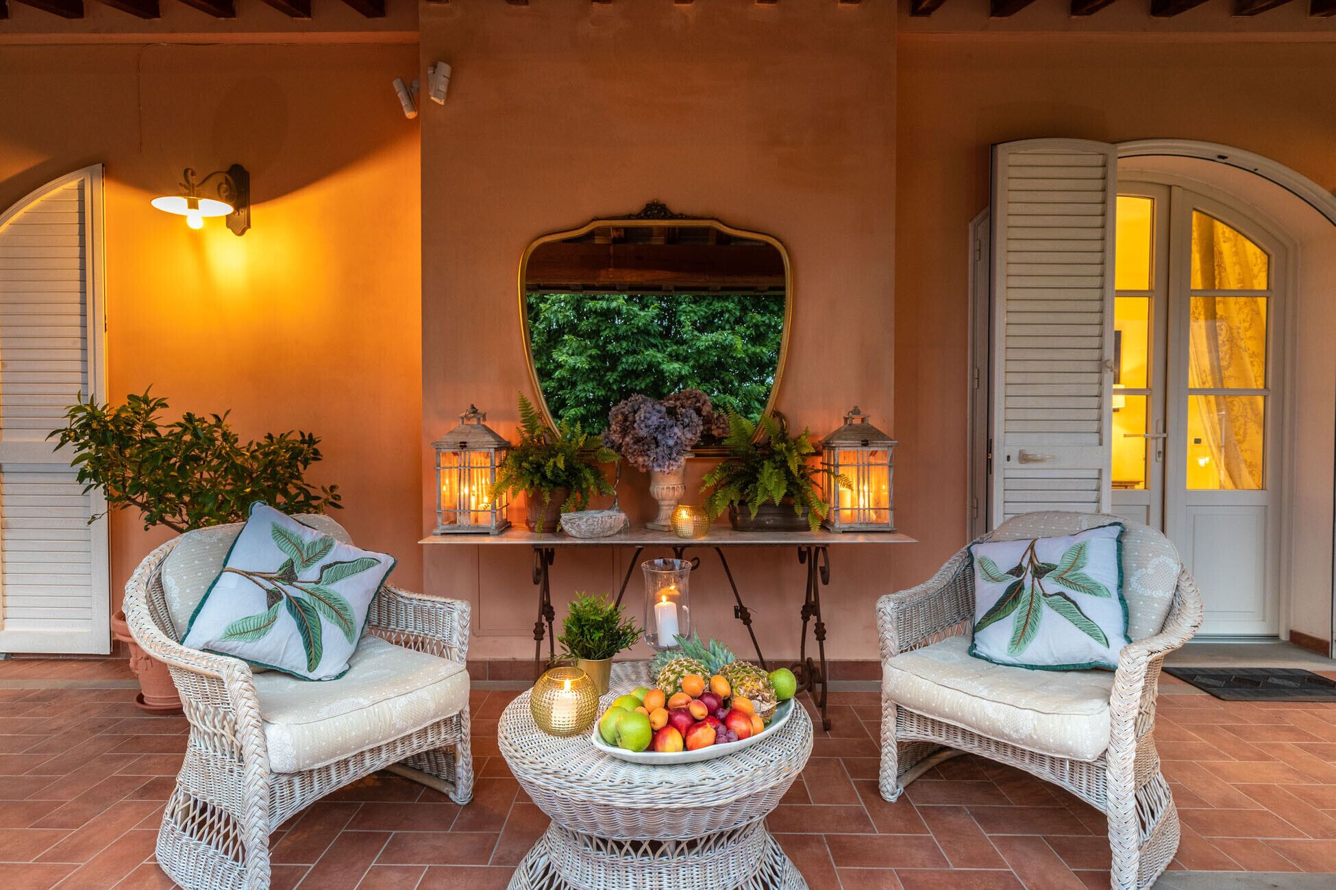 Un espace extérieur accueillant avec des fauteuils en osier, un panier de fruits et des lanternes décoratives.