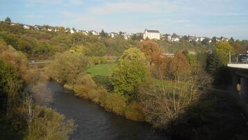 Une rivière traverse un paysage verdoyant, avec un pont et un grand bâtiment en arrière-plan.