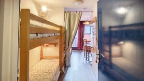 Un pasillo estrecho con una litera a la izquierda, una puerta a la derecha y una ventana con cortinas al fondo.