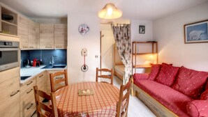 Una habitación compacta con kitchenette, una mesa de comedor con sillas, un sofá rojo y una cama pequeña.