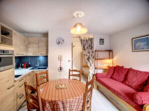 Una habitación compacta con kitchenette, una mesa de comedor con sillas, un sofá rojo y una cama pequeña.