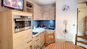 Una cocina compacta con armarios de madera, horno integrado, microondas, pileta y una mesa de comedor con mantel a cuadros.