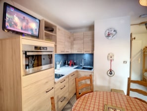 Una cocina compacta con armarios de madera, horno integrado, microondas, pileta y una mesa de comedor con mantel a cuadros.