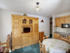 A room with a wooden cabinet, a television, a dining table, and a kitchen area with a microwave. - Les Menuires: 3 rooms, 5 pers, 30m², ski-in/ski-out (Les Menuires)