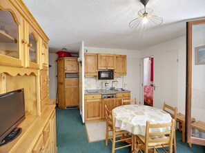 A compact kitchen with wooden cabinets, a microwave, and a dining area with a table and chairs. - Les Menuires: 3 rooms, 5 pers, 30m², ski-in/ski-out (Les Menuires)