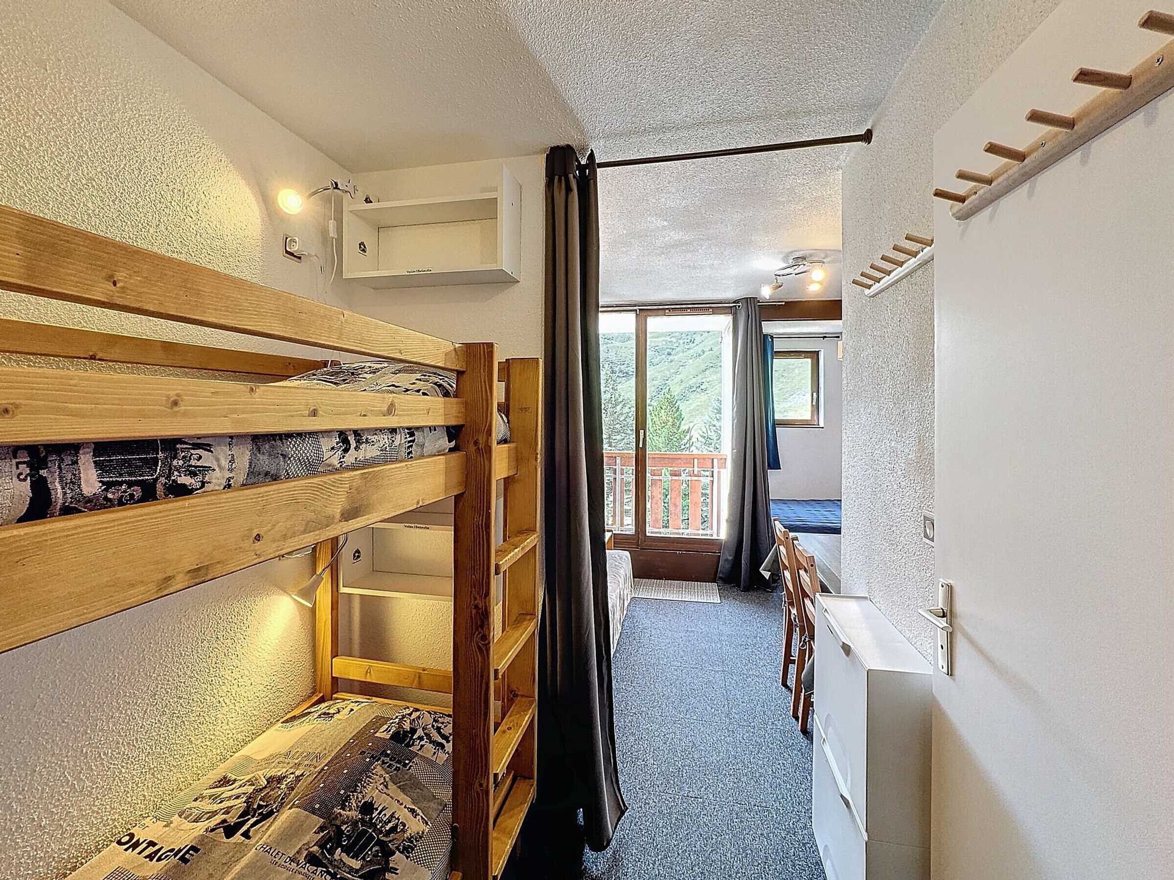 A compact room with a bunk bed, a small window, and a door leading to a balcony.