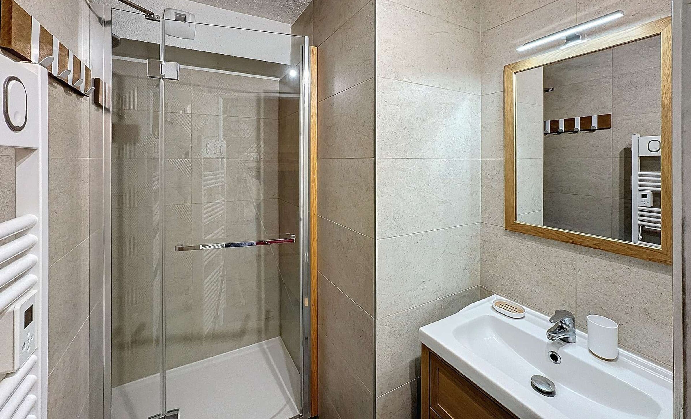 A modern bathroom with a glass shower enclosure, a white sink with a mirror, and a towel rack.