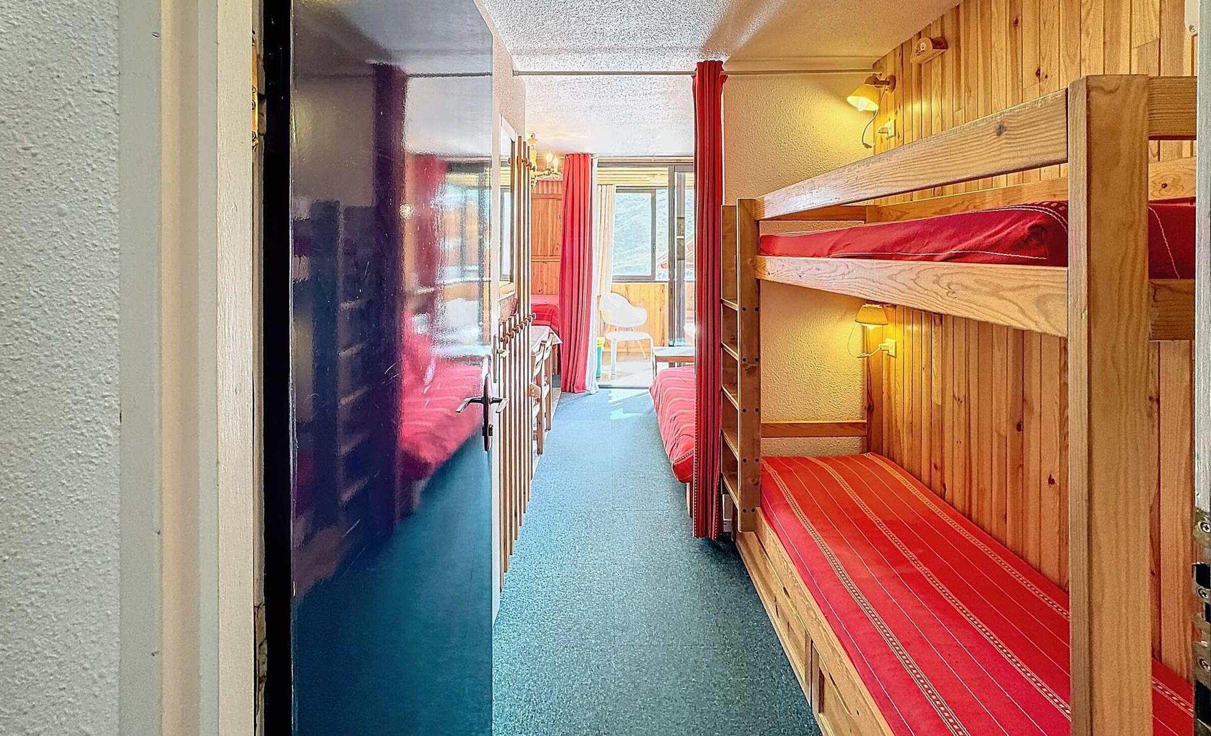Ein schmaler Gang mit Etagenbetten an einer Seite, Holzwänden und einem Fenster am Ende.