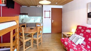 A compact room with a wooden ceiling, a kitchenette, a dining area with a table and chairs, a sofa with patterned cushions, and a door. - Cozy studio 4 pax - Station center in La Clusaz (La Clusaz)