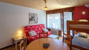 A cozy room with a wooden ceiling, a red sofa with heart patterns, a bunk bed, a small table, and a ceiling fan. - Cozy studio 4 pax - Station center in La Clusaz (La Clusaz)