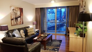 A modern living room with a leather sofa, a coffee table, and a large window with a city view. -  Luxury 2 bedroom apartment Sydney, Darling Harbour, ICC and free secure parking (Sydney)