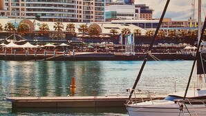 A marina with boats docked, a large hotel building in the background, and a waterfront promenade with umbrellas. -  Luxury 2 bedroom apartment Sydney, Darling Harbour, ICC and free secure parking (Sydney)