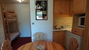 Une cuisine compacte avec des meubles en bois, un four à micro-ondes et un évier. Une table ronde en bois, entourée de chaises, se trouve au centre de la pièce.