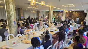 Un evento formal con mesas redondas, asistentes sentados y cabina de DJ.