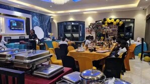 Un salón de banquetes con mesas dispuestas para una comida, una araña y una pantalla de televisión.