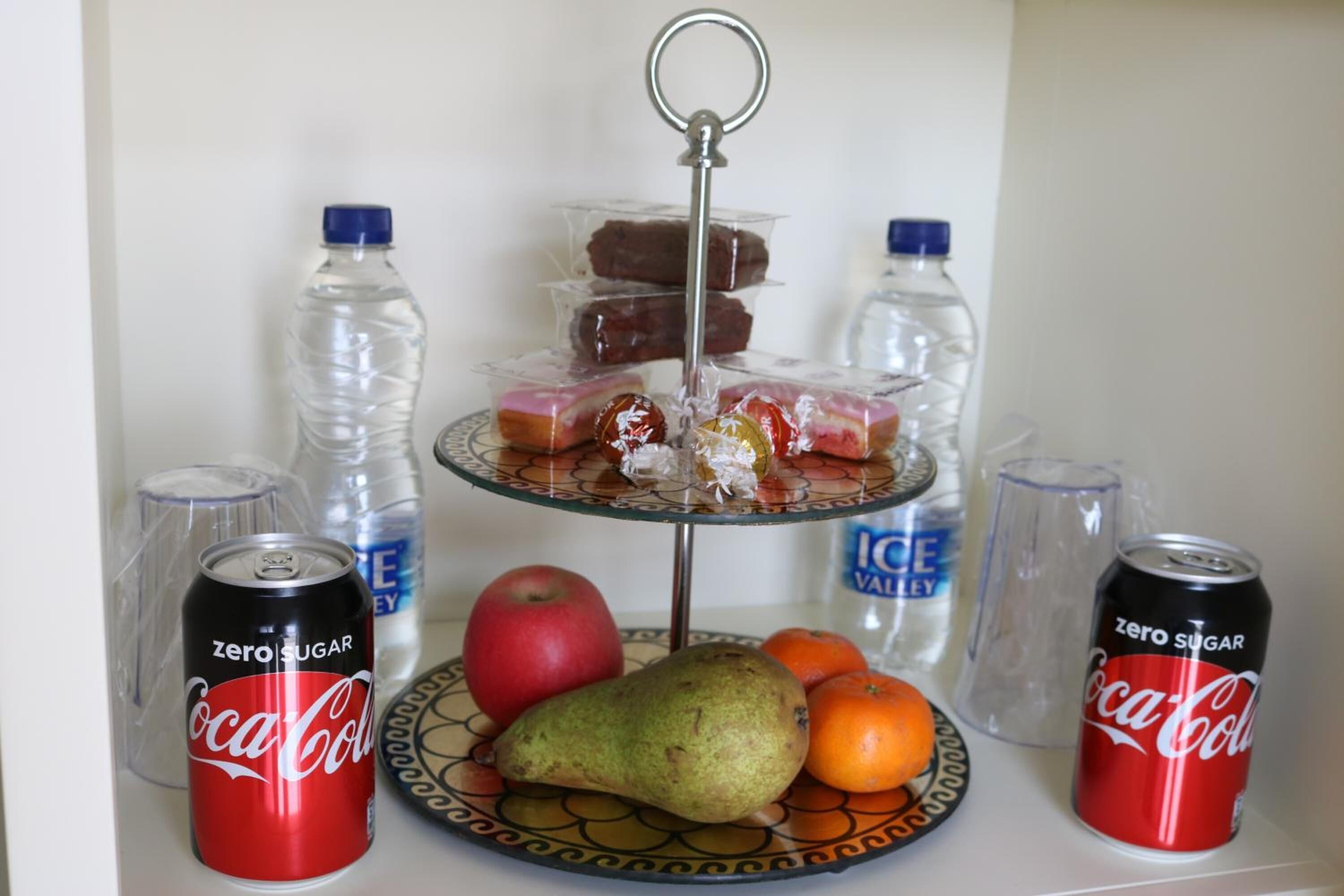 Un plateau de collations comprenant des fruits et des chocolats, deux canettes de Coca-Cola et deux bouteilles d’eau.