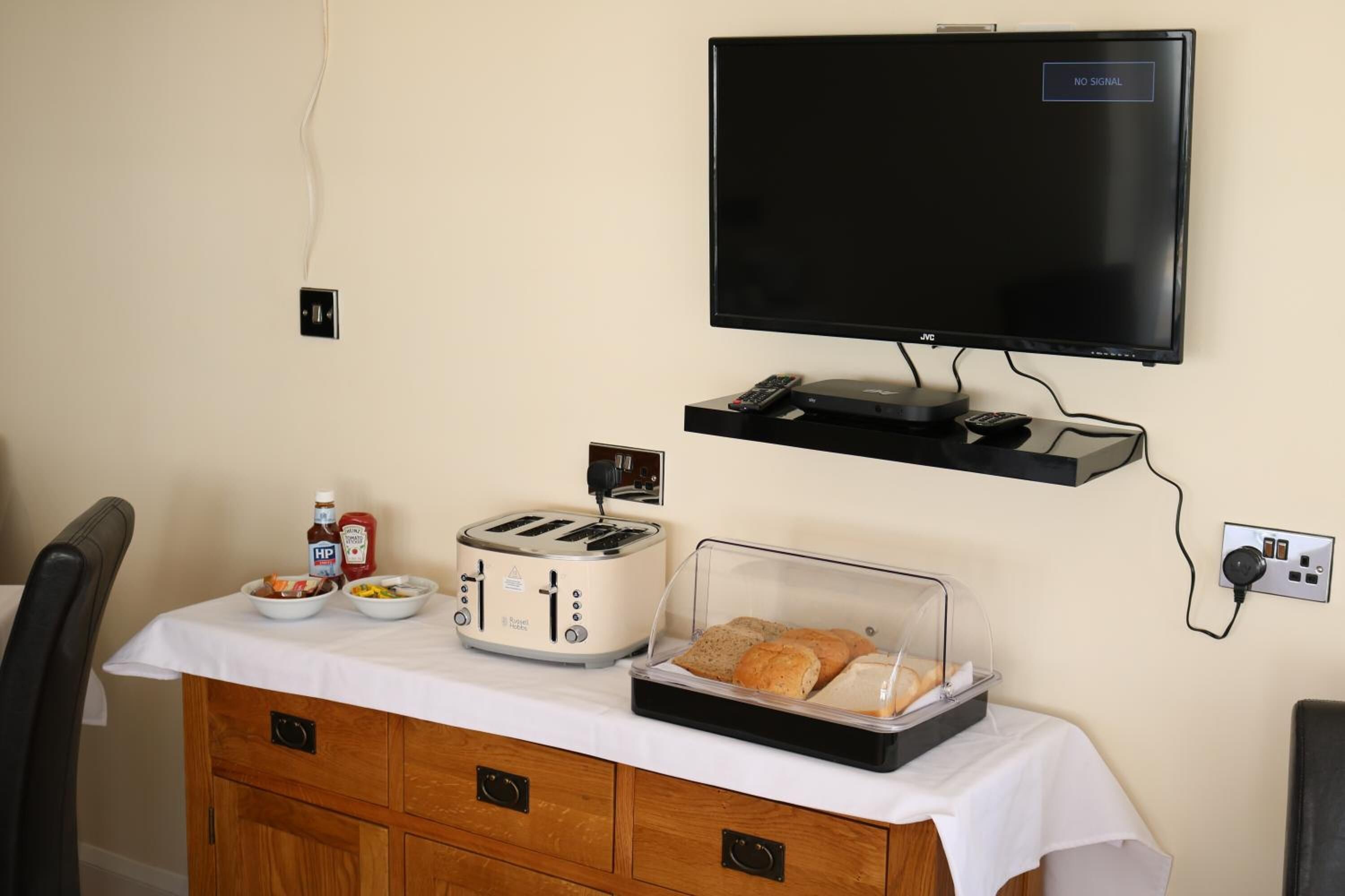 Uma cozinha compacta com torradeira, cesta de pão e televisão de tela plana na parede.