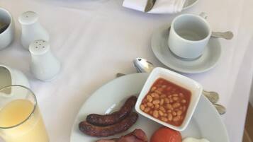 A breakfast setting with plates of sausages, beans, bacon, eggs, and toast, along with cups of coffee and a glass of orange juice.