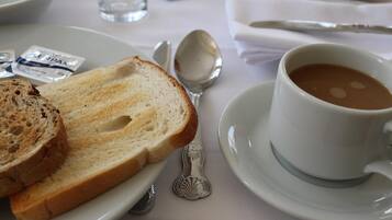 Colazione servita con pane tostato, una tazza di caffè e un cucchiaio su un tavolo.