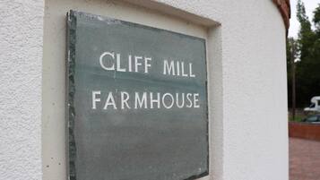 Un letrero con la inscripción 'CLIFF MILL FARMHOUSE' colgado en una pared.