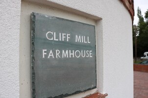 Un letrero con la inscripción 'CLIFF MILL FARMHOUSE' colgado en una pared.