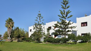 Un bâtiment moderne doté de nombreux balcons, entouré d’un espace verdoyant bien entretenu et de palmiers.