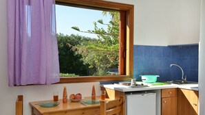 Une cuisine de taille réduite avec une table en bois, une fenêtre ornée d’un rideau violet, un évier et un égouttoir à vaisselle.