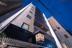 A modern hotel with multiple floors, a prominent 'HOTEL ANN' sign, and a clear blue sky.