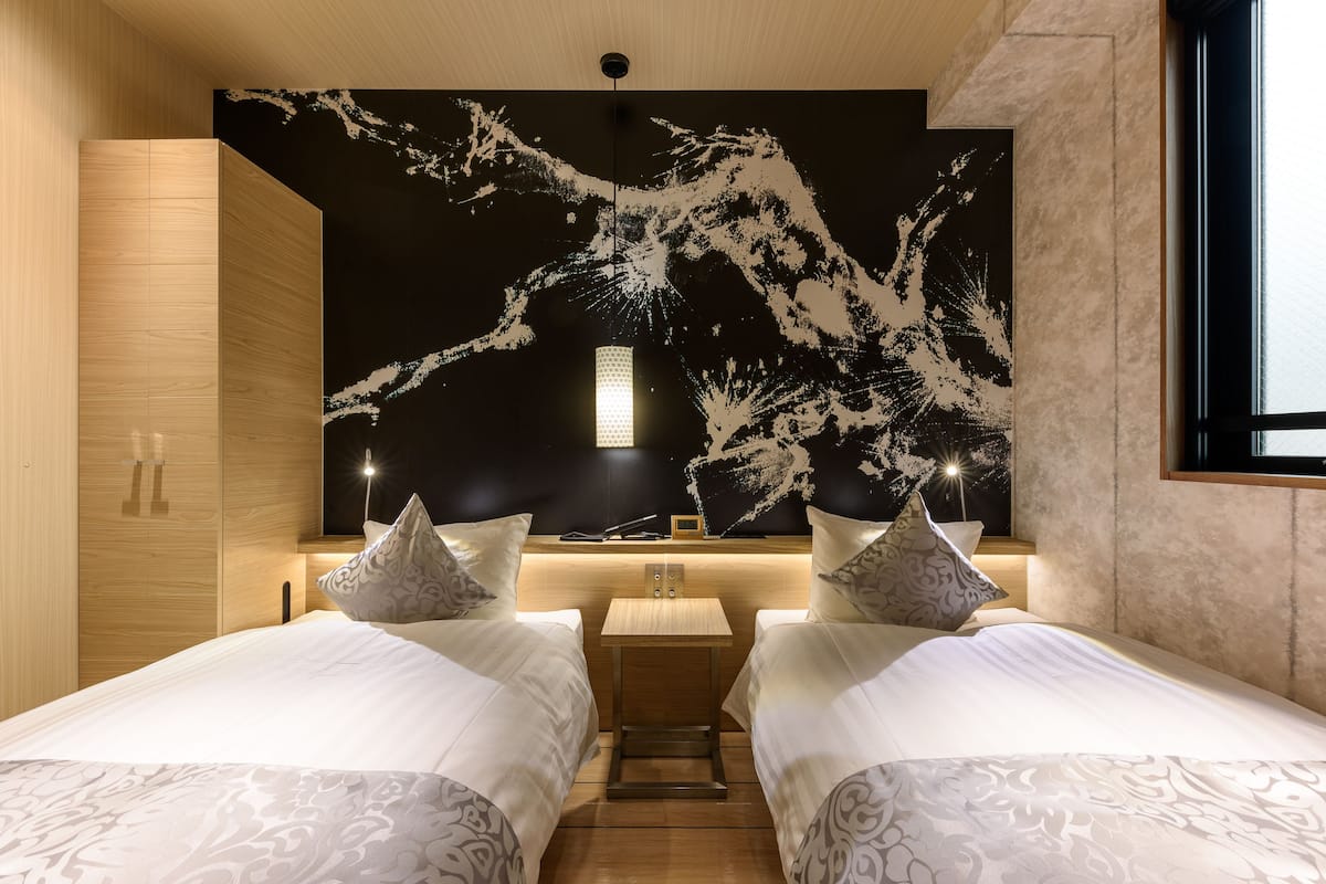 A modern hotel room with two beds, a nightstand, and a large abstract wall mural.