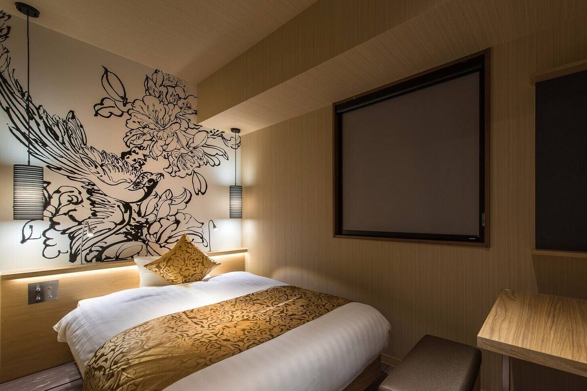 A hotel room with a large bed, a wall-mounted TV, a desk, and a decorative wall mural.