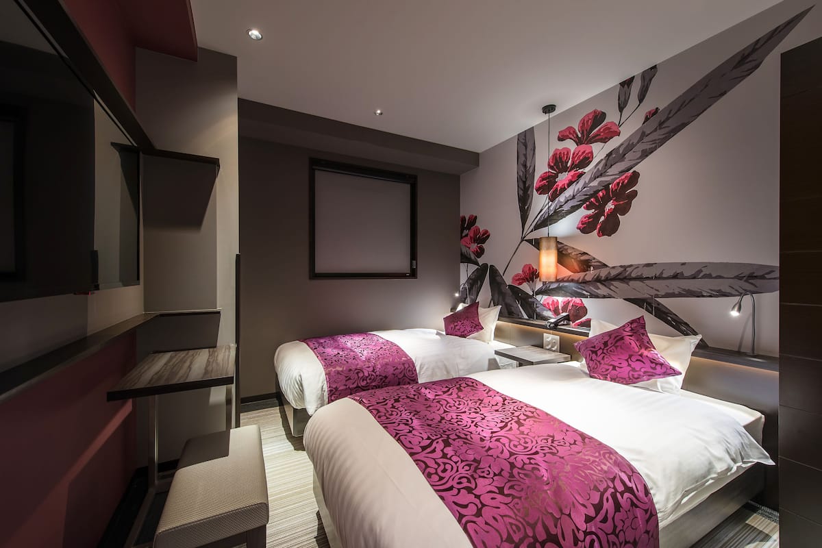 A modern hotel room with two beds, a large mirror, and a decorative wall with a floral pattern.