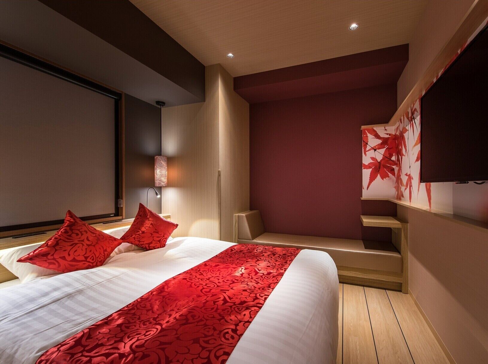 A modern hotel room with a large bed, red patterned bedspread, and a seating area with a red leaf wall art.