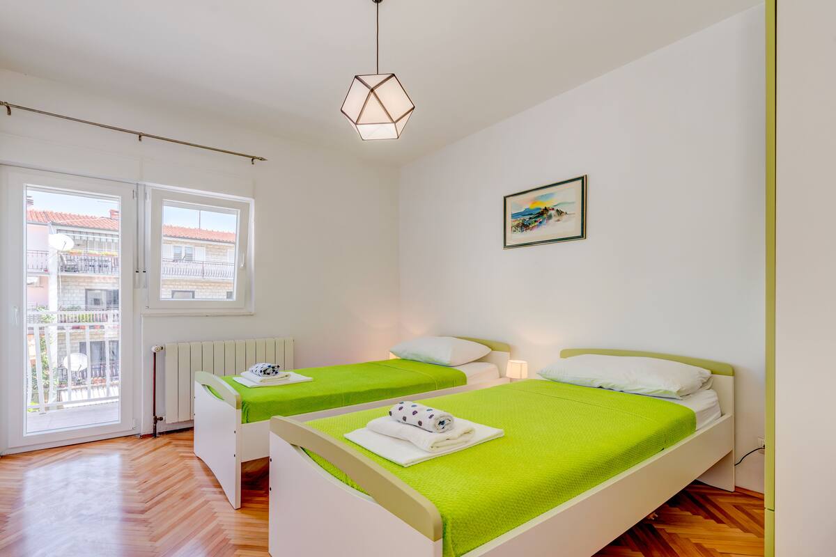 A hotel room with two beds, a radiator, a window, and a hanging light fixture.