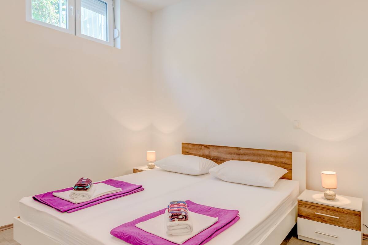 A modern bedroom with a large bed, two bedside tables, and a window with blinds.